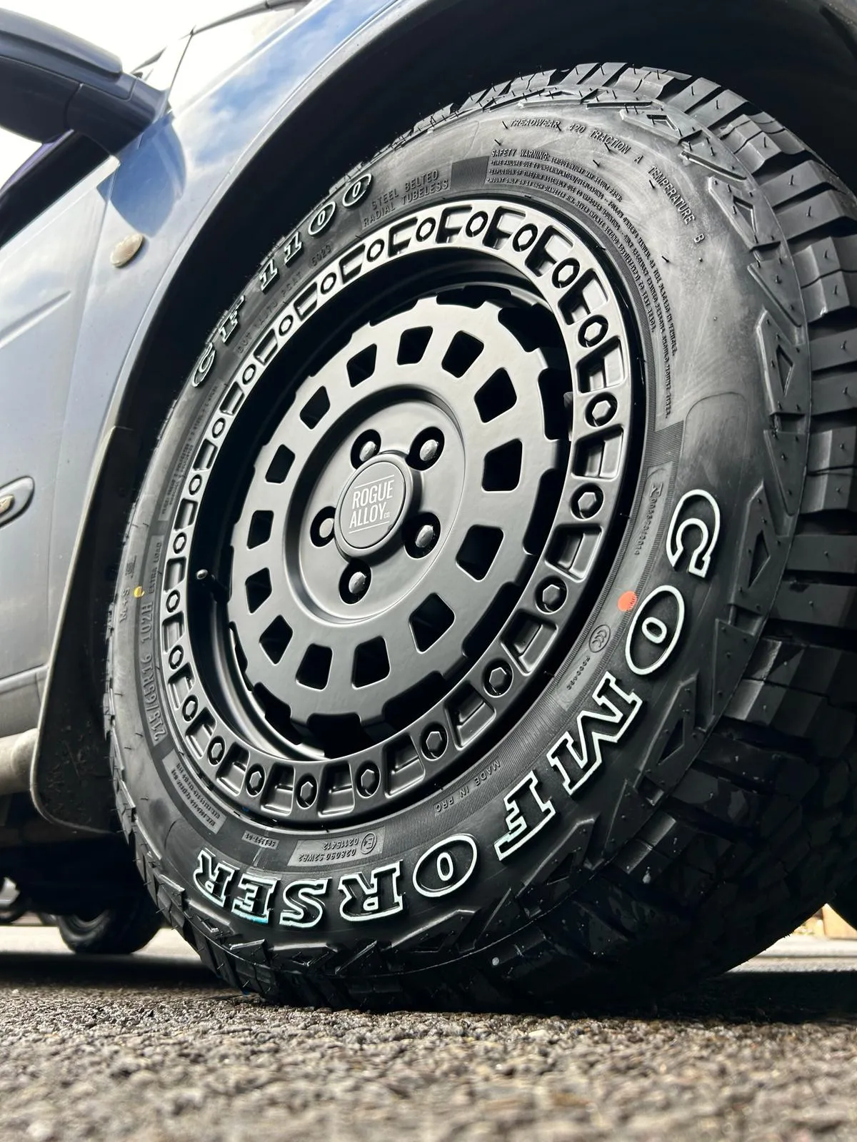 Close-up of a Comforser all-terrain tire mounted on an SUV, showing the tread pattern and alloy wheel.